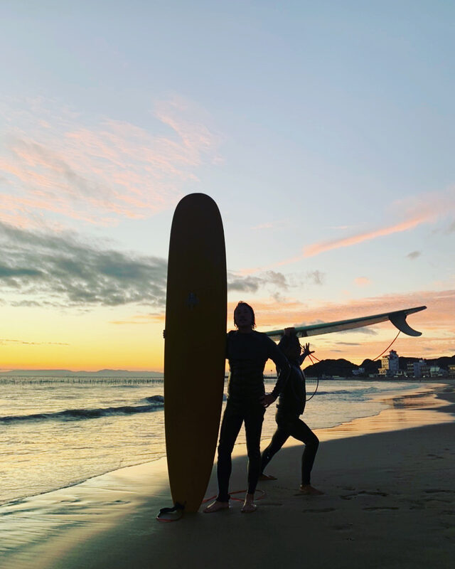夕暮れの海辺でサーフボードを持つ二人